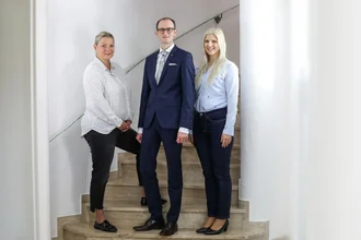 Drei Mitglieder der Geschäftsleitung von der Denkströme auf einer Treppe – professionell, zukunftsorientiert, sympathisch – Businessportrait in heller Umgebung