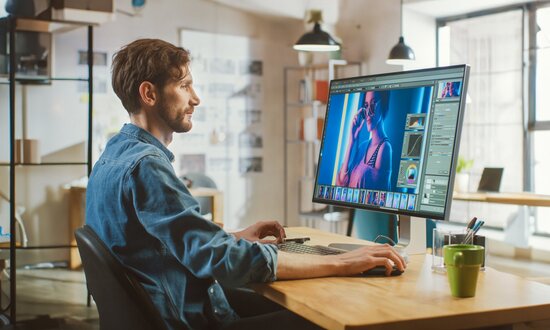 Kreativdesigner arbeitet konzentriert an einem großen Bildschirm mit Bildbearbeitungssoftware in modernem Büro – steht für digitales Design, visuelle Kommunikation und kreative Medienproduktion