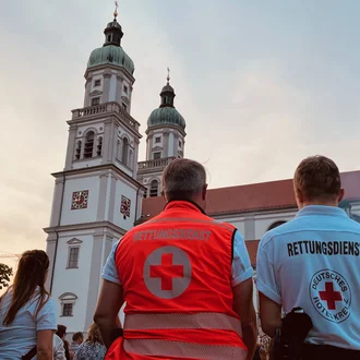 Zwei Einsatzkräfte des Rettungsdienstes vom Deutschen Roten Kreuz stehen vor historischer Kirche bei Großveranstaltung im Freien – Sanitätsdienst und Sicherheit im öffentlichen Raum