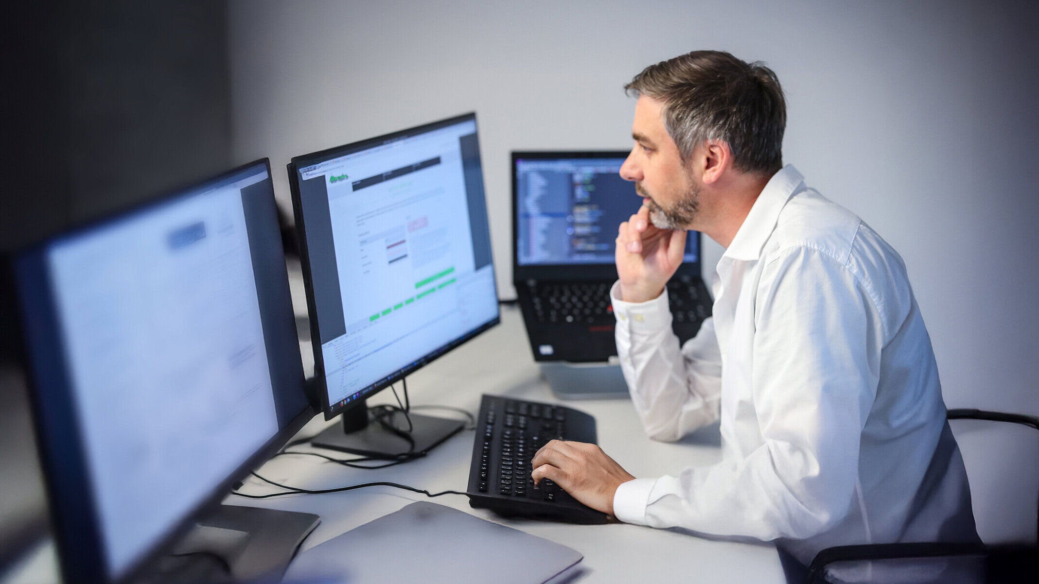 Denkströme IT-Spezialist arbeitet konzentriert an mehreren Monitoren – Softwareentwicklung und Programmierung im modernen Büro