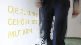 Person geht dynamisch an Wand mit motivierendem Schriftzug ‚Die Zukunft gehört den Mutigen‘ im Denkströme Büro vorbei