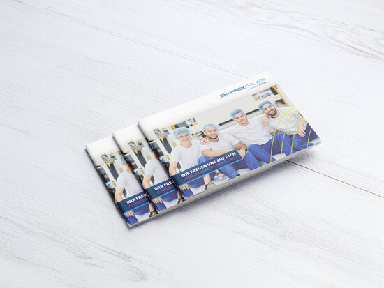Gedruckte Ausbildungsbroschüren von EK-Pack Folien auf hellem Holztisch – Titelbild zeigt vier junge Auszubildende in Arbeitskleidung mit Haarnetz, lächelnd vor einer Produktionsanlage. Aufschrift: „Wir freuen uns auf dich – Ausbildung bei EK-Pack Folien“