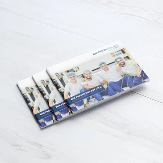 Gedruckte Ausbildungsbroschüren von EK-Pack Folien auf hellem Holztisch – Titelbild zeigt vier junge Auszubildende in Arbeitskleidung mit Haarnetz, lächelnd vor einer Produktionsanlage. Aufschrift: „Wir freuen uns auf dich – Ausbildung bei EK-Pack Folien“