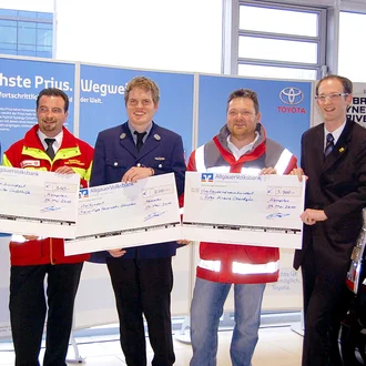Spendenübergabe im Autohaus: Fünf Männer in Uniform und Anzug überreichen symbolische Spendenschecks – aufgenommen 2011, unter anderem mit Vertretern des Roten Kreuzes und der Feuerwehr