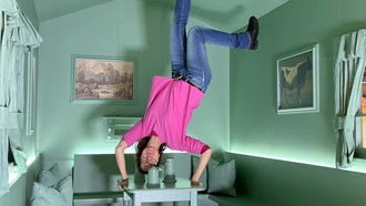 Mitarbeiterin  im pinken Shirt steht scheinbar kopfüber auf dem Tisch in einem grünen Raum – Perspektivspiel und kreative Illusion bei Denkströme Event