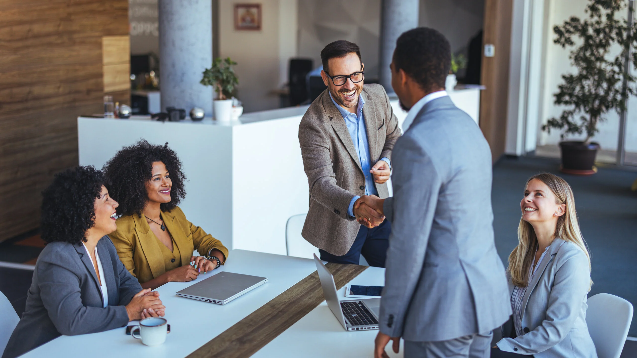 Geschäftsleute begrüßen einen neuen Gesprächspartner per Handschlag in einem modernen Besprechungsraum.