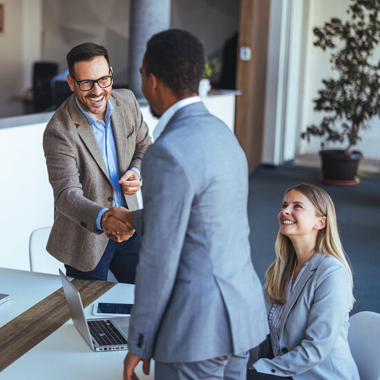 Geschäftsleute begrüßen einen neuen Gesprächspartner per Handschlag in einem modernen Besprechungsraum.