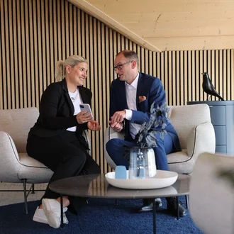 Geschäftsleitung von Denkströme im Gespräch: Zwei Führungskräfte sitzen in einem Lounge-Bereich, schauen auf ein Smartphone und besprechen Inhalte.