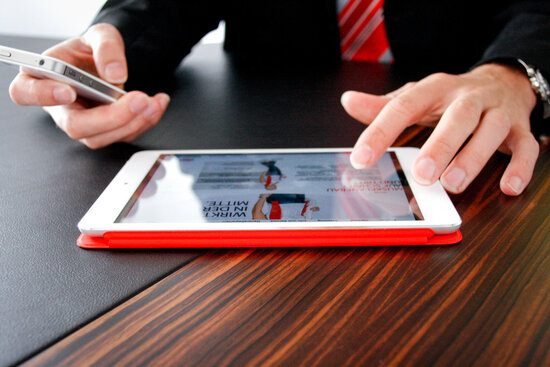 Denkströme Mitarbeiter im Anzug nutzt Tablet und Smartphone am Konferenztisch für moderne digitale Kommunikation.
