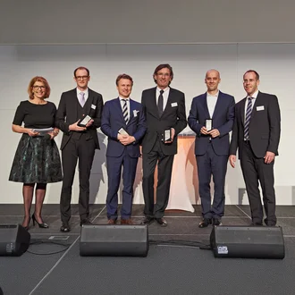 Gruppenfoto der Preisträger beim Exzellenzpreis 2018 – sechs Geschäftsleute in Businesskleidung mit Auszeichnung auf Bühne, festlicher Veranstaltungsrahmen mit Rednerpult und Mikrofonen