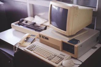 Alter Desktop-Computer mit Röhrenmonitor, Tastatur, Maus, Floppy-Disk, Nadeldrucker und Festnetztelefon auf einem Schreibtisch – Retro-Technologie aus den 1980er-Jahren