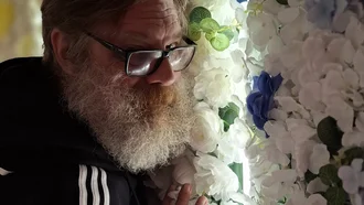 Mitarbeiter mit Bart und Brille steht lächelnd vor einer Wand aus weißen Kunstblumen bei Denkströme Event