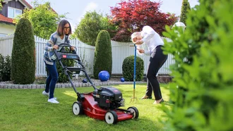 Zwei Mitarbeiterinnen der Denkströme bei der Gartenarbeit: eine mit Rasenmäher, die andere mit Gartenwerkzeug – Spaß bei der Arbeit im Grünen