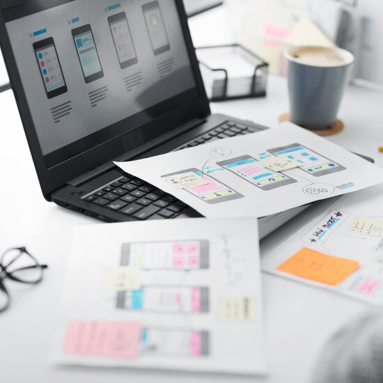 UX-Designerin entwickelt Wireframes und mobile App-Prototypen mit Skizzen und Laptop – kreative Konzeptarbeit im digitalen Produktdesign
