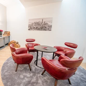 Eleganter Besprechungsraum mit roten Designersesseln, rundem Tisch, Kaminfeuer und stilvoller Dekoration im Satellite Office München Hopfenstraße