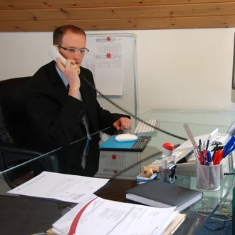 Büroszene aus dem Jahr 2008: Mann im Anzug telefoniert am Schreibtisch mit iMac und Glasplatte, modernes Büro mit Felge als Designelement