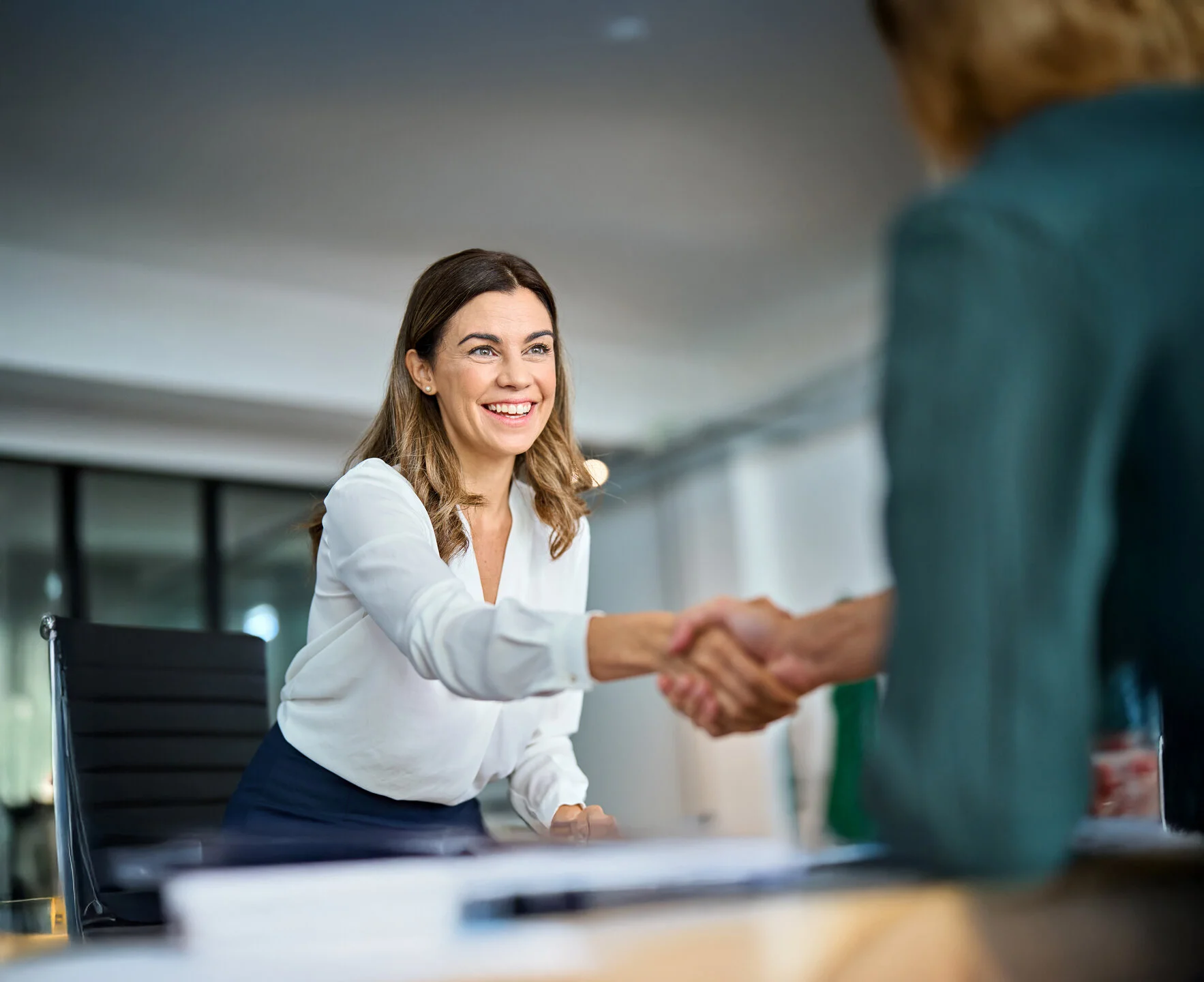 Bewerberin begrüßt eine Person per Handschlag bei einem Gespräch im modernen Büro.