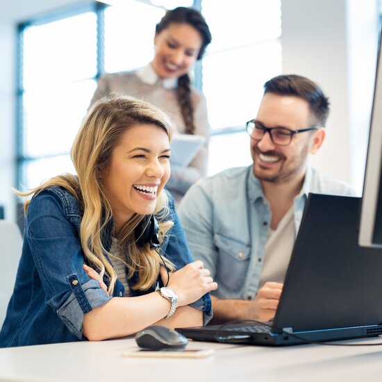 Engagiertes Fullstack-Entwicklungsteam bei der Arbeit im modernen Büro – junge Kolleg:innen lachen gemeinsam beim Coding und Projektmanagement am Bildschirm im Rahmen einer digitalen Transformationsberatung