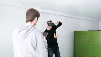 Denkströme IT-Entwickler mit VR-Brille testet virtuelle Realität im Büro der Denkströme Gruppe, betreut von Kollege mit Tablet – Symbol für innovative Digitalentwicklung und immersive Technologien