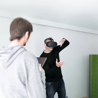 Denkströme IT-Entwickler mit VR-Brille testet virtuelle Realität im Büro der Denkströme Gruppe, betreut von Kollege mit Tablet – Symbol für innovative Digitalentwicklung und immersive Technologien