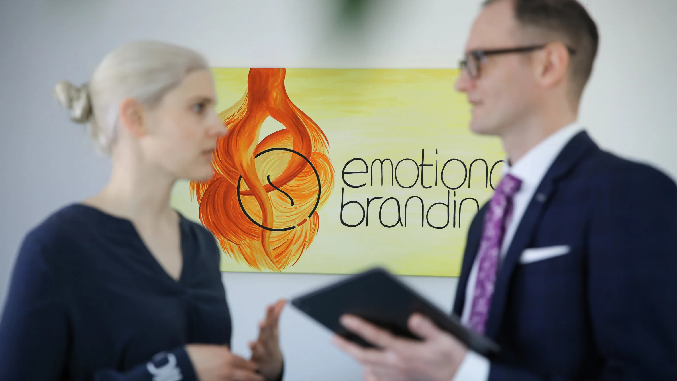 Denkströme Geschäftsführerin und Geschäftsführer im Gespräch vor Logo mit der Aufschrift ‚emotional branding‘ – professionelle Kommunikation über Markenstrategie und visuelle Identität
