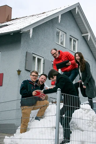 Junges kreatives Team lacht gemeinsam im Schnee vor einem Bürogebäude – Teamspirit und Arbeitskultur bei Denkströme im Winter 2015