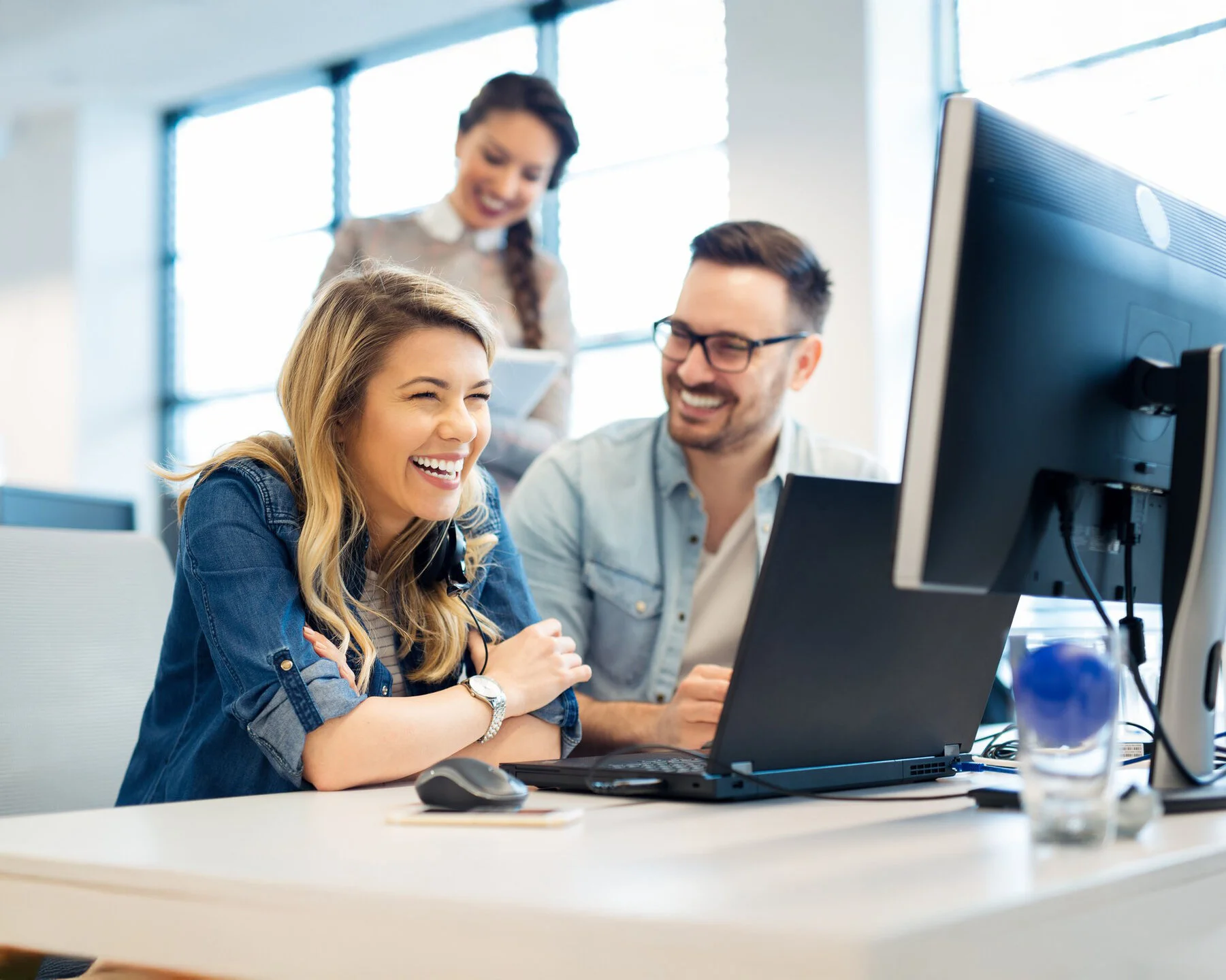 Lachendes Entwicklerteam bei der Zusammenarbeit im modernen Büro – Fullstack-Developer und Kolleg:innen am Computer bei agiler Projektarbeit in der Transformationsberatung