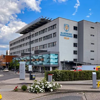 Außenansicht des Allgemeinen Krankenhauses Celle mit neuer Fassadengestaltung, Logo an der Wand und Rettungswagen im Einsatzbereich
