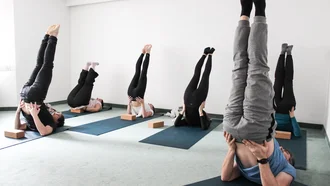 Gruppe von Mitarbeitenden bei gemeinsamer Yoga-Einheit in Schulterstand-Position – Gesundheitsförderung am Arbeitsplatz