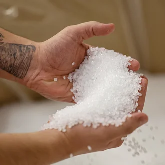 Nahaufnahme von Händen mit Tätowierung, die weiße Kunststoffgranulat-Pellets halten – Rohmaterial für die Kunststoffverarbeitung in der Industrieproduktion
